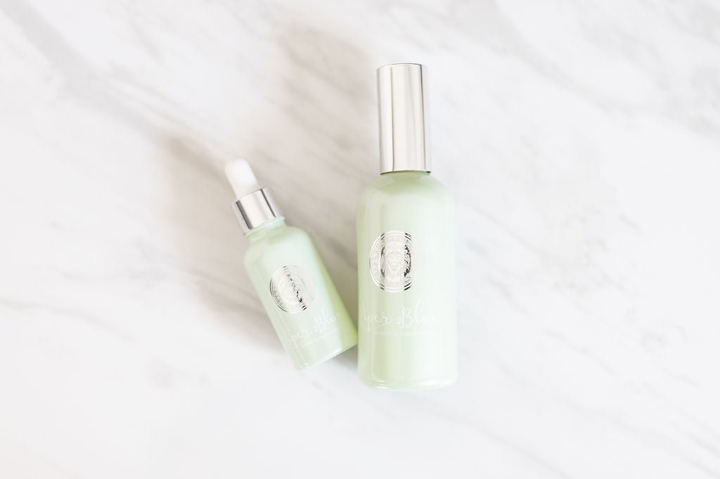 Large bottle of Ageless Skin Cleanser and smaller dropper bottle of serum set on a marble background.