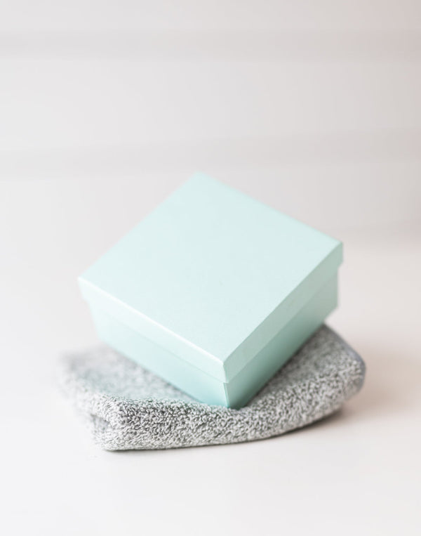 Small light blue box on a grey textured makeup remover cloth  with a blurred white background