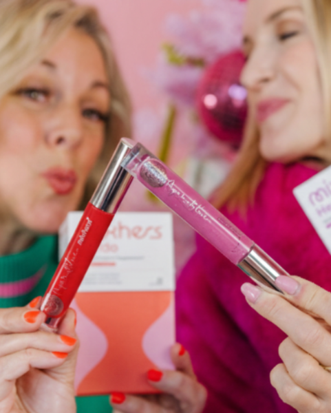 Two women holding lip gloss products with a blurred background