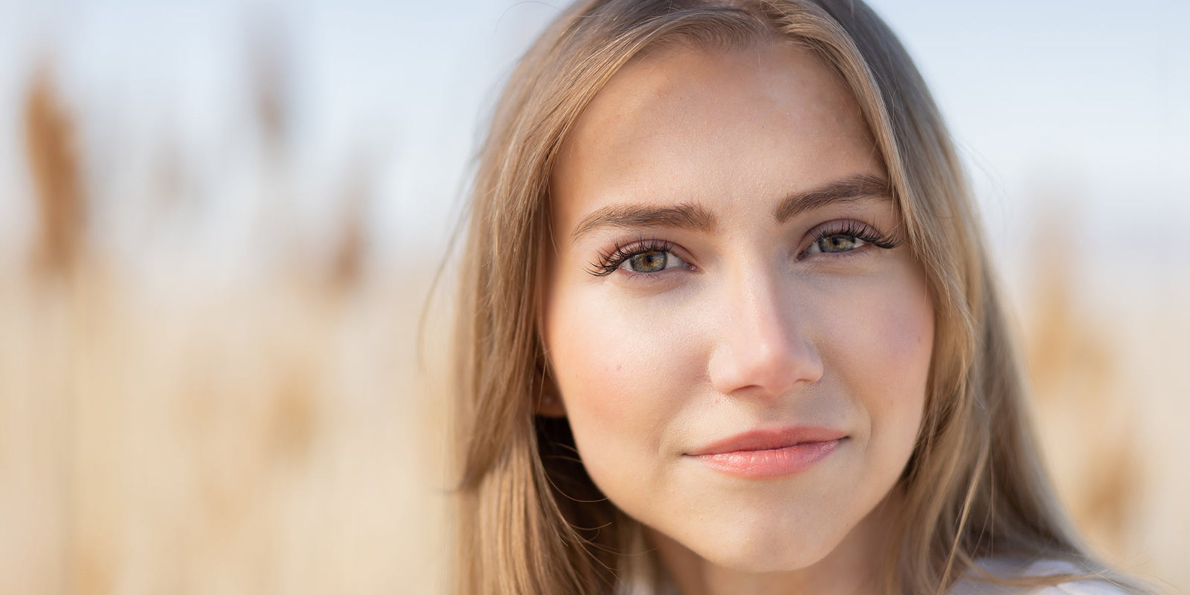 Close-up of a woman with blonde hair and blue eyes against a blurred natural background