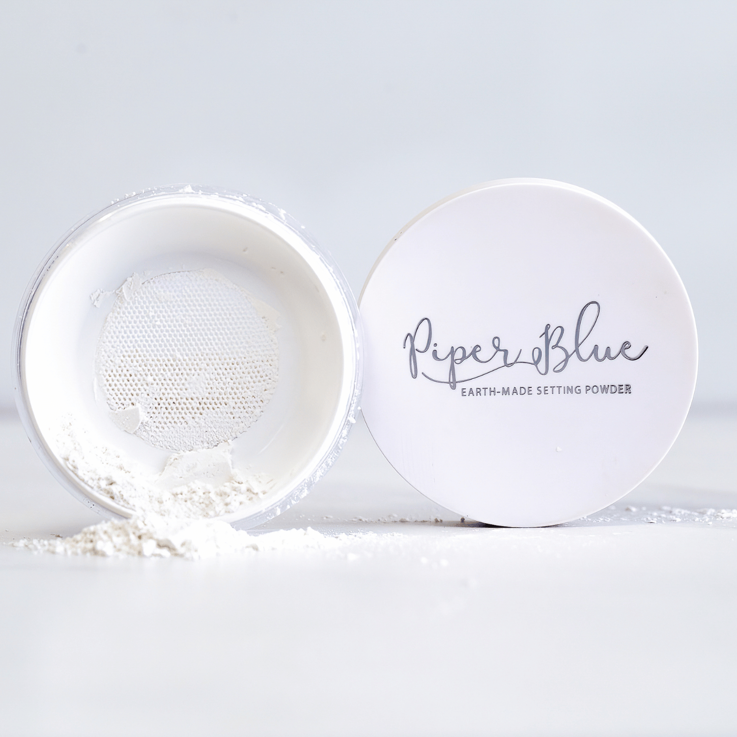 A jar of PiperBlue earth-made setting powder is open with powder visible inside. The product is labeled as 'PiperBlue' and 'Earth-Made Setting Powder'.