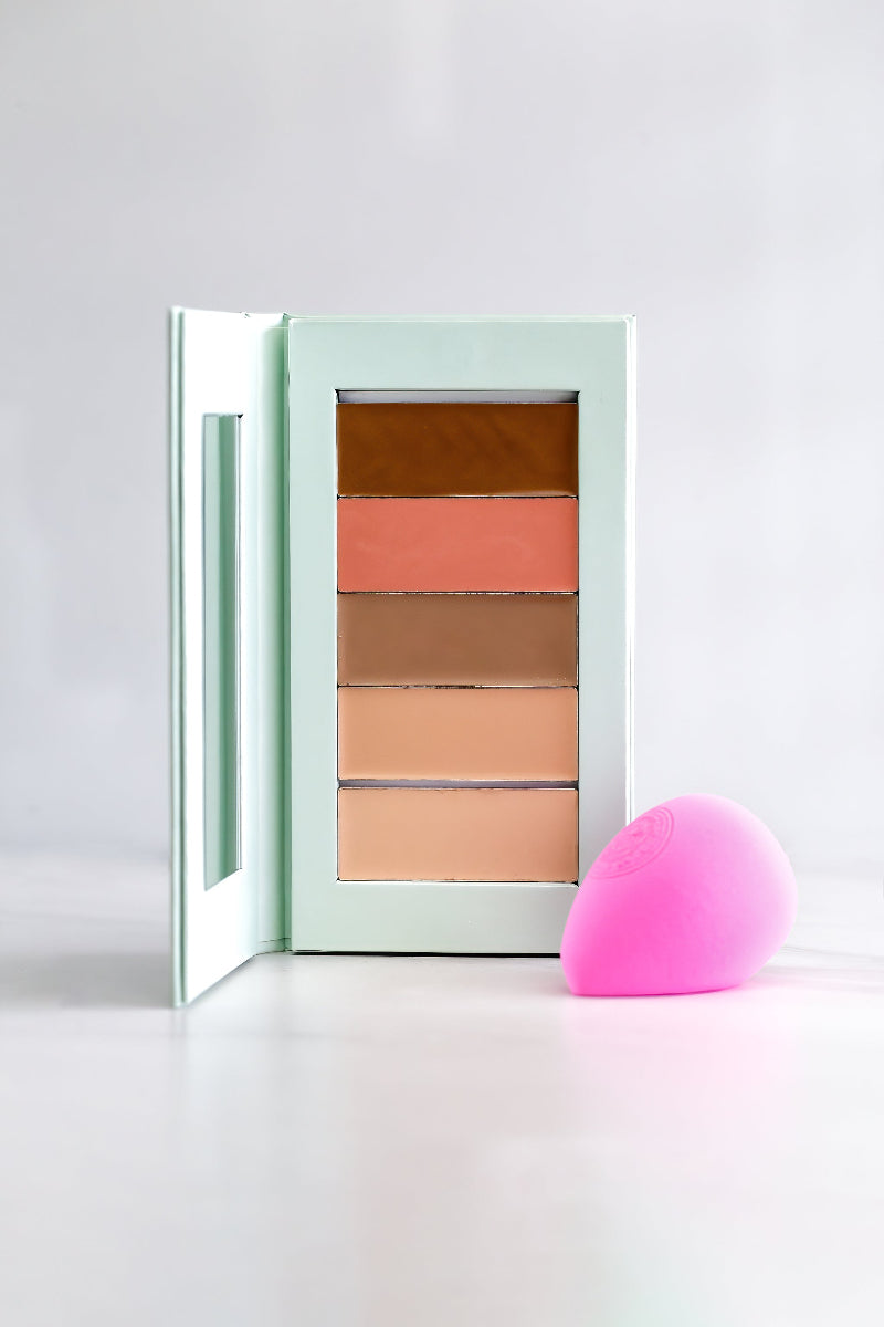 An open compact palette with various makeup shades and a pink microfiber makeup blender