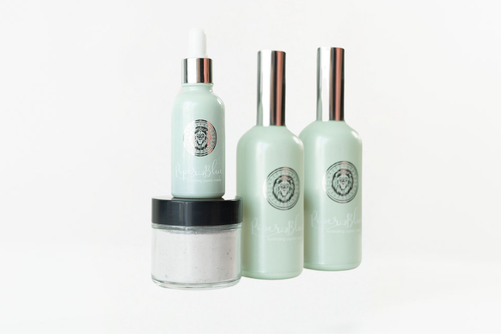 A collection of skincare products including a cleanser, serum, setting spray, and an exfoliating scrub, arranged on a white surface.